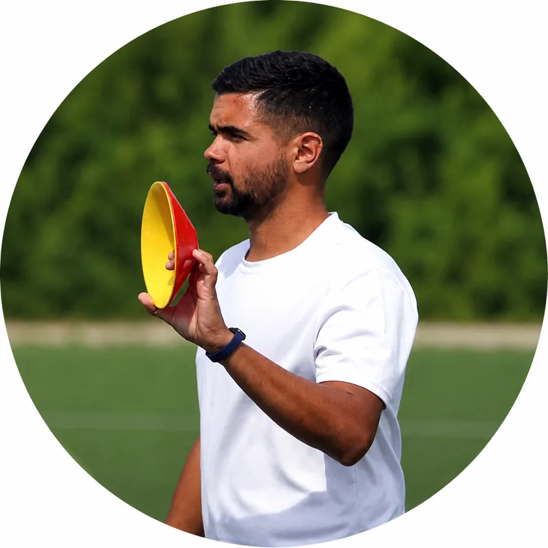 João Rangel de t-shirt branca, a segurar um disco de treino amarelo e vermelho num campo ao ar livre.