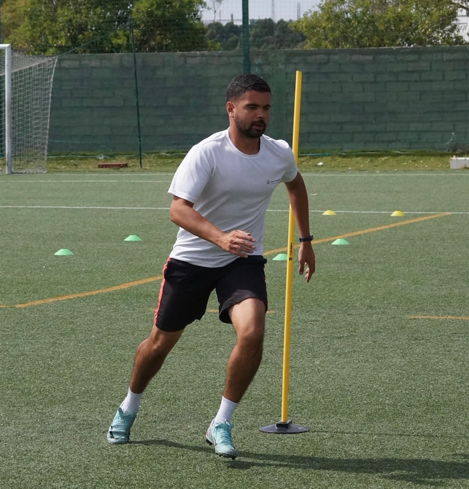 Jogador em exercício de agilidade com barreiras num treino individual ao ar livre.
